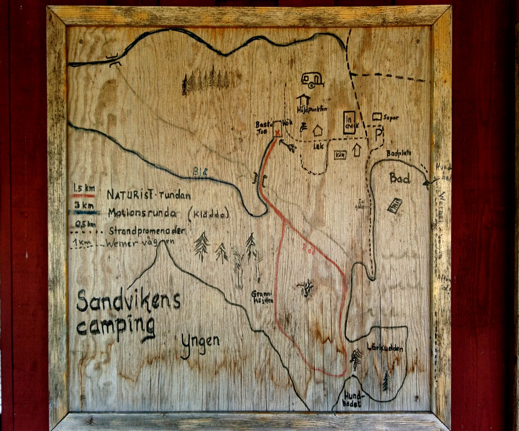 Le plan du camp, peint sur du bois, est affiché sur le mur d'une maison avec le rouge typique des maisons en bois suédoises. Le « Motionsrunda » (tour d'exercice) doit être effectué en klädda (vêtements) (1/15)